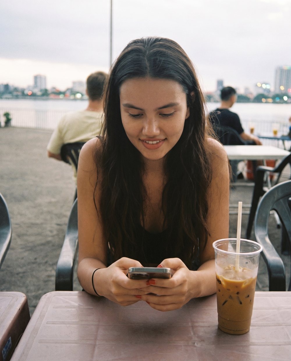 A woman at a riverside cafe typing a message on her phone