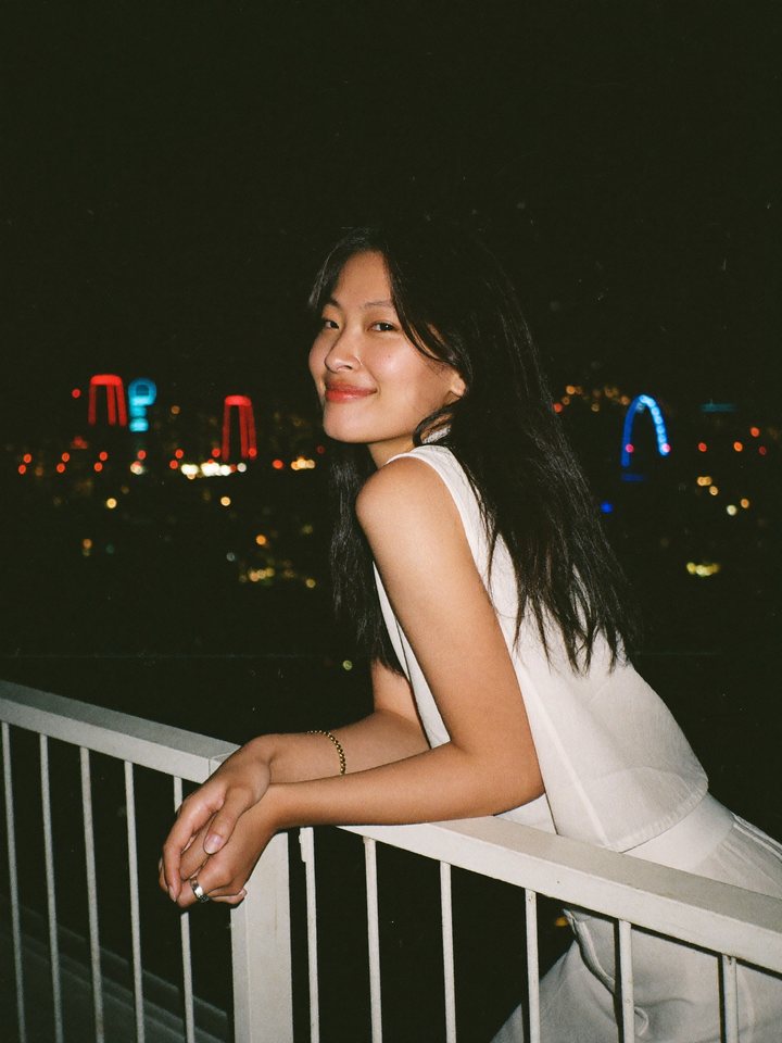 A woman leaning on a rooftop railing above the city at night