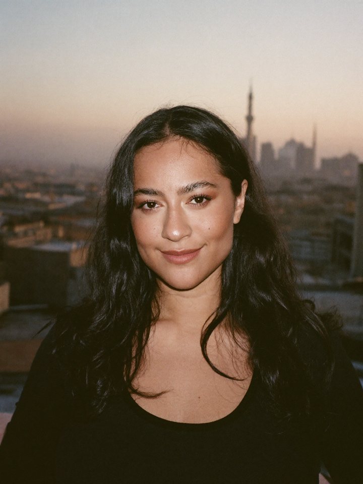 A woman on a rooftop at sunset looking calmly into the camera