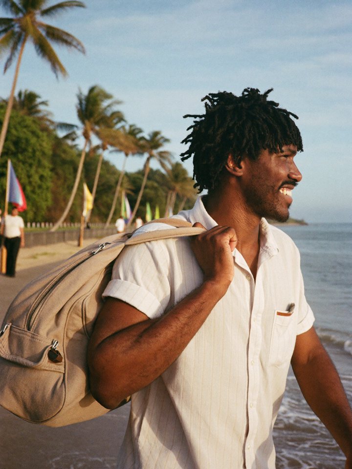 A man walking along the seafront at golden hour with a travel bag