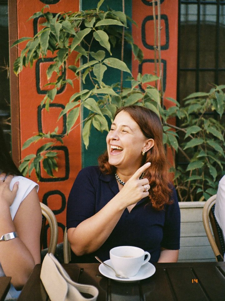 A woman laughing mid-conversation at a sidewalk cafe