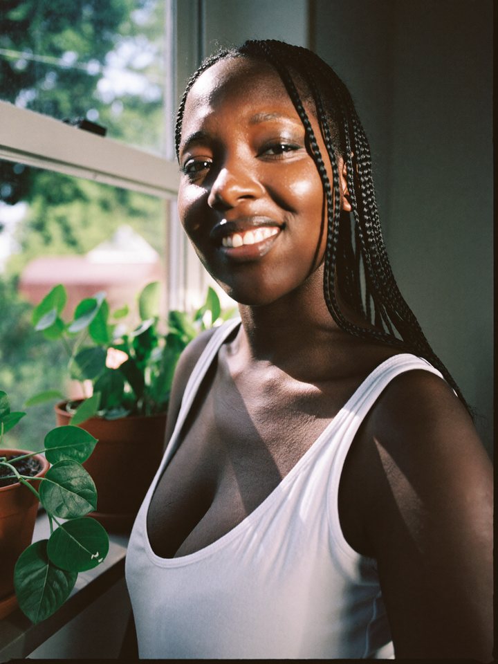 A woman by a sunny window looking into the camera with a warm smile