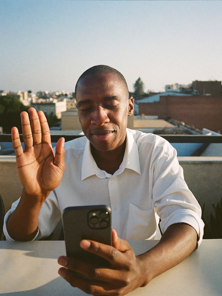 A man giving a relaxed wave on a video call at a rooftop table at golden hour